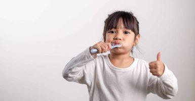 Little cute child girl brushing her teeth on white background. Space for text. Healthy teeth.