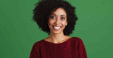 Black young woman wearing sweater smiling and looking at camera isolated over green background